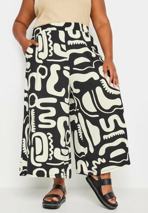 Pantalons larges noir et crème avec des motifs abstraits, dotés d'une taille élastique et de poches latérales. Tissu doux avec une coupe décontractée.