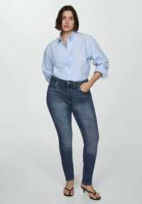 Svetlo modra srajca s gumbi, temno modri skinny kavbojki in črne sandale s peto. Obleka ima sproščen kroj in mehak denim material.