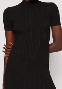 Robe noire côtelée à manches courtes et col montant. Texture lisse avec des rayures verticales, ajustée au corps, silhouette cintrée.