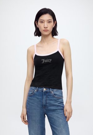 Giovane donna con capelli corti e scuri che indossa una canottiera nera con spalline rosa e testo "Juicy", abbinata a jeans blu a vita alta.