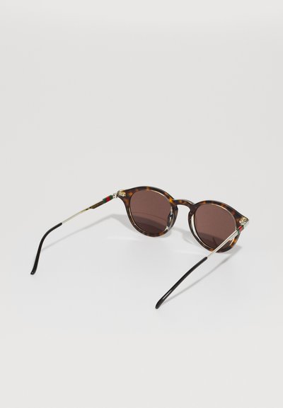 Lunettes de soleil rondes en écailles de tortue avec des verres foncés et des branches métalliques fines présentant des rayures vertes et rouges près des charnières.