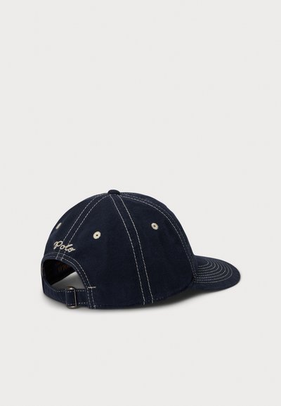 Temno modra baseball kapa z vezenim logotipom, ukrivljenim šiltom, šest panelno zasnovo in belimi šivi. Nastavljiv trak na hrbtni strani.