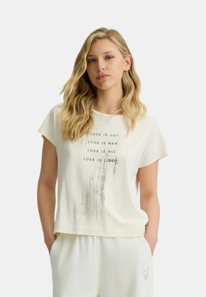 T-shirt bianco a maniche corte con una vestibilità ampia, caratterizzato da testo argento che mostra frasi "LOVE IS" e un dettaglio a gradiente testurizzato.