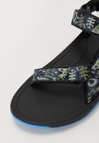 Sorte sandaler med mønstrede tekstilremmer i blått, grønt og svart. Har en teksturert fotseng og en blå såleakse.