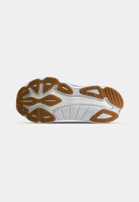 Semelle de chaussure en caoutchouc blanc et marron avec une bande de roulement à motif et le nom de la marque Saucony embossé au centre.