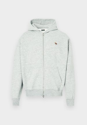 Šedá mikina na zips vyrobená z mäkkej látky, s predným zipsom a malým vyšitým logom zvieraťa na hrudi. Obsahuje kapucňu a vrecká.