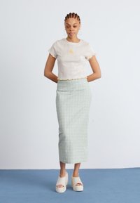 Vit ribbad crop top med solbroderi, matchad med en ljusgrön rutmönstrad midikjol och vita platåskor.