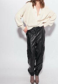 Krémový pletený cardigan s hlubokým výstřihem do V a dvěma knoflíky, doplněný černými vysokým pasem koženými kalhotami ve stylu cargo s elastickými lemy.