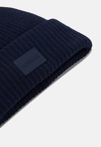 Námořnická pletená čepice s ribbed vzorem, se čtvercovou gumovou nášivkou loga BOGNER na manžetě. Měkká tkanina a těsný střih.