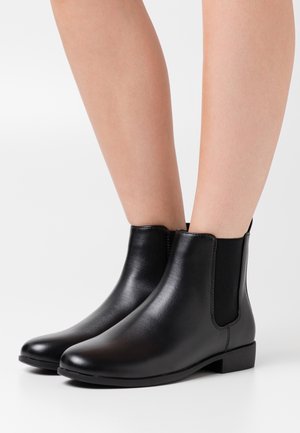 Black ankle boots made of smooth leather with elastic side panels, a rounded toe, and a low textured heel.