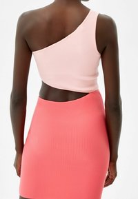 Asymmetrisk ribbad topp i ljusrosa med ärmlös design, matchad med en figurnära korallfärgad ribbad minikjol. Slät textur genom hela plagget.