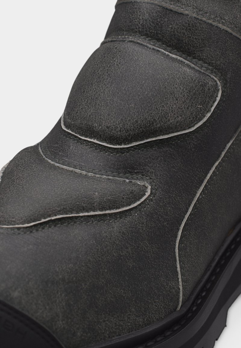 Close-up of black leather shoe with reinforced padded areas and visible stitching on the upper part of the sole.