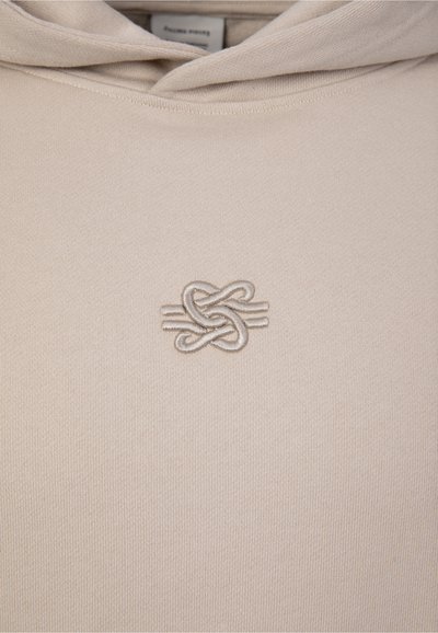 Sweat à capuche beige avec un design abstrait de nœud brodé subtil centré sur la poitrine, juste en dessous de l'encolure.