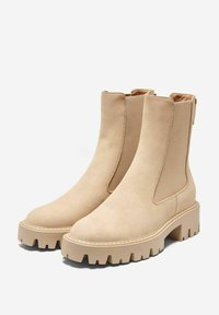 Bottes cheville beiges en suede lisse avec des panneaux élastiques sur les côtés, semelles en caoutchouc épaisses et un design à bout rond.