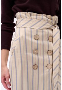 Beige gestreepte rok met lichtblauwe en rode verticale lijnen, drie houten knopen, een tailleband en een zijzak.