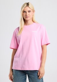 Pink cotton t-shirt with short sleeves and a round neck. Features a white embroidered logo on the left side of the chest. Casual fit.