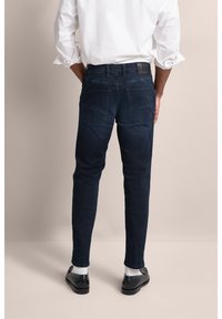 Granatowe dżinsy wykonane z denimu, w slim fit, o gładkiej strukturze. Posiadają dwie tylne kieszenie oraz skórzaną metkę marki blisko pasa.