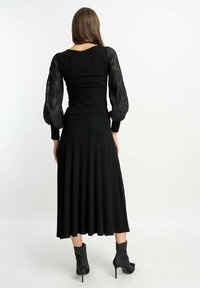 Czarna sukienka z dopasowanym gorsetem i rozkloszowanym spódnicą, z przezroczystymi, kwiatowymi, bufkami oraz długością do kostek. Czarne botki na obcasie.