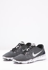 Nike atletik sko i sort med en mesh-overdel, med en grå swoosh, hvidsprættet mellemsål og sorte snørebånd. Letvægtsdesign.