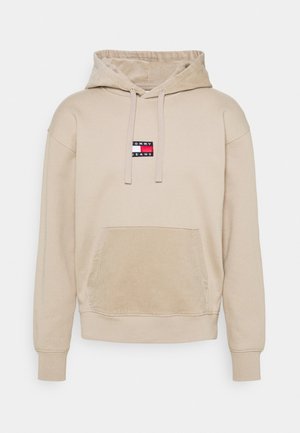 Beige värihuppari, jossa etutasku ja kiristysnyörillinen huppu. Rinnassa pieni suorakaiteen muotoinen Tommy Jeansin logo punaisena, valkoisena ja laivastonsinisenä.