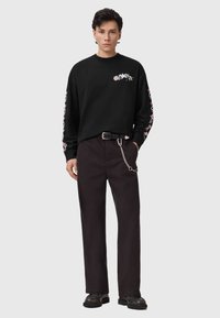 Top negro de manga larga con estampados gráficos coloridos en las mangas, combinado con pantalones oscuros que tienen un detalle de cadena en el cinturón. Calzado negro.