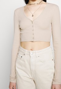 Top court côtelé beige à manches longues, avec un col en V et huit boutons. Associé à un jean blanc taille haute.