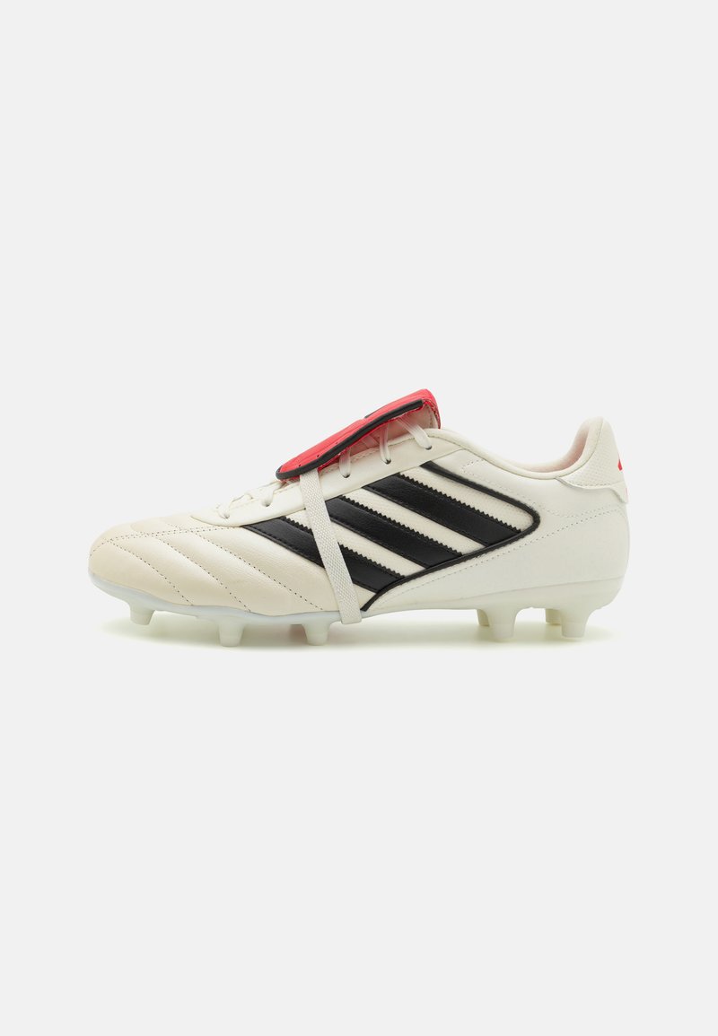 Chuteira de futebol branca com riscas pretas, parte superior de couro texturizado, design com atacadores, detalhe vermelho na língua e pinos de borracha brancos na sola.
