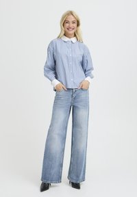 Blauw-wit gestreepte blouse met een witte kraag, gecombineerd met lichtblauwe wijde jeans en zwarte pump met puntige neuzen.