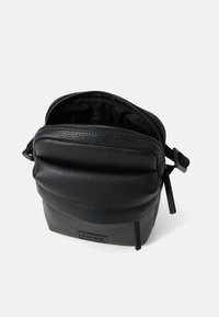 Černá kožená crossbody taška s texturovaným povrchem, zipovým uzávěrem a nastavitelným popruhem. Vnitřek je podšívkovaný hladkým materiálem.