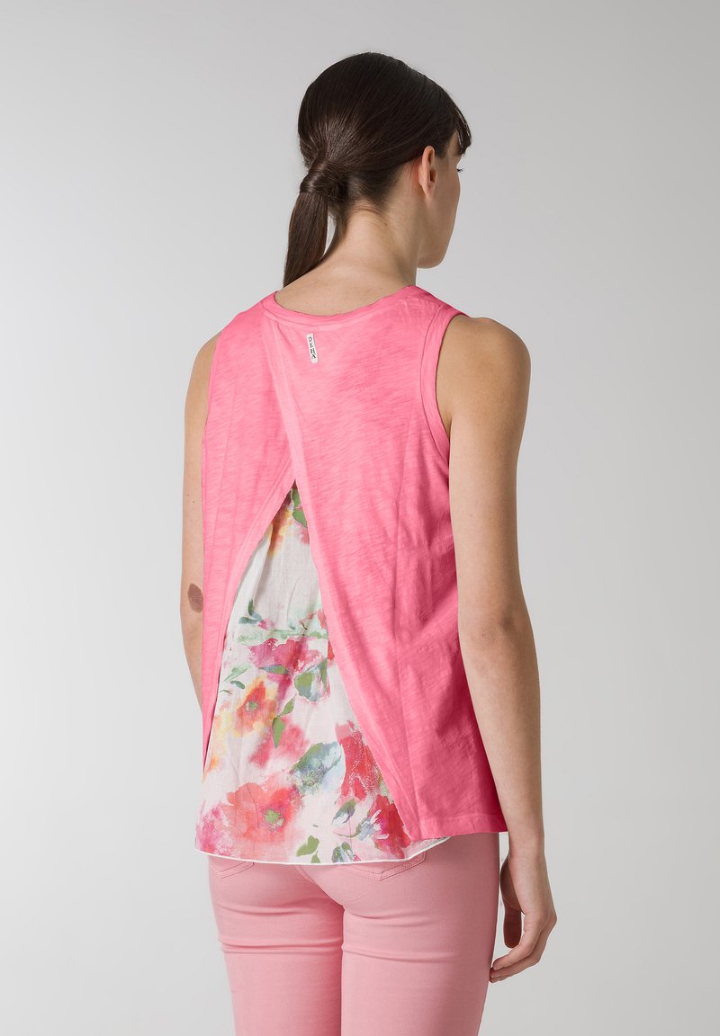 Rosa ärmlös topp med ett blommönstrat innerlager som syns genom en spricka i ryggen. Mjuk textur och avslappnad design.
