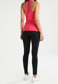 Top deportivo rosa con diseño de espalda nadadora y leggings negros con un patrón texturizado. Zapatillas blancas completan el atuendo.