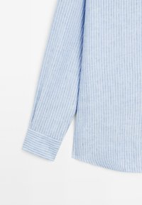 Camicia a righe azzurro chiaro con maniche lunghe, dotata di polsini con bottoni e una vestibilità rilassata. Realizzata in un tessuto testurizzato.