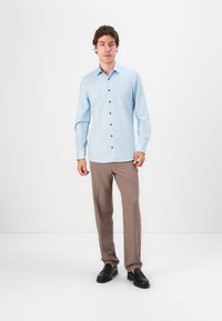 Light blue button-up shirt with long sleeves, dark buttons, paired with light brown trousers and black loafers. Simple, tailored fit.