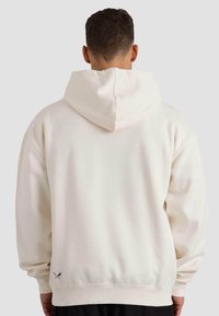 Sudadera blanca con capucha, de corte relajado, tejido texturizado y puños de canalé. Presenta un pequeño logo en el dobladillo.