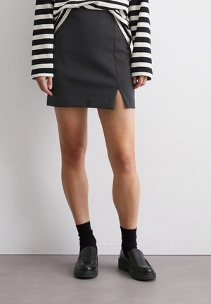 Jupe mini noire avec une fente avant, associée à un haut à rayures noires et blanches à manches longues et des mocassins noirs avec des chaussettes. Texture lisse.