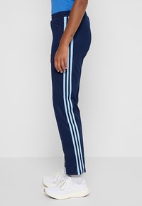 Tmavomodré športové nohavice s svetlomodrými pruhmi po bokoch, s úzkym strihom a bočnými vreckami, vyrobené z jemnej látky.