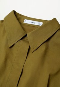 Chemise vert olive à col avec patte de boutonnage cachée et étiquette de marque visible MNG à l’intérieur de l’encolure.