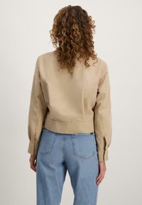 Khaki kort jasje met opgeblazen mouwen, een zachte textuur en een aansluitende taille, gecombineerd met lichtblauwe denim jeans.