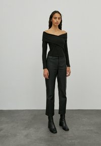 Schwarzes Off-Shoulder-Top mit gerafftem Stoff, kombiniert mit hochgeschnittenen schwarzen Lederhosen und Stiefeletten, alles strukturiert und figurbetont.