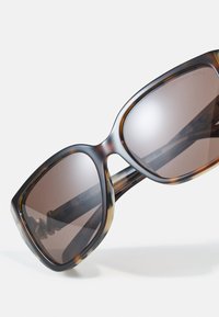 Ochelari de soare cu model țestoasă, cu lentile mari și rotunde. Lentile de un brun închis cu un gradient și un cadru din plastic lucios, neted, cu un design îndrăzneț.