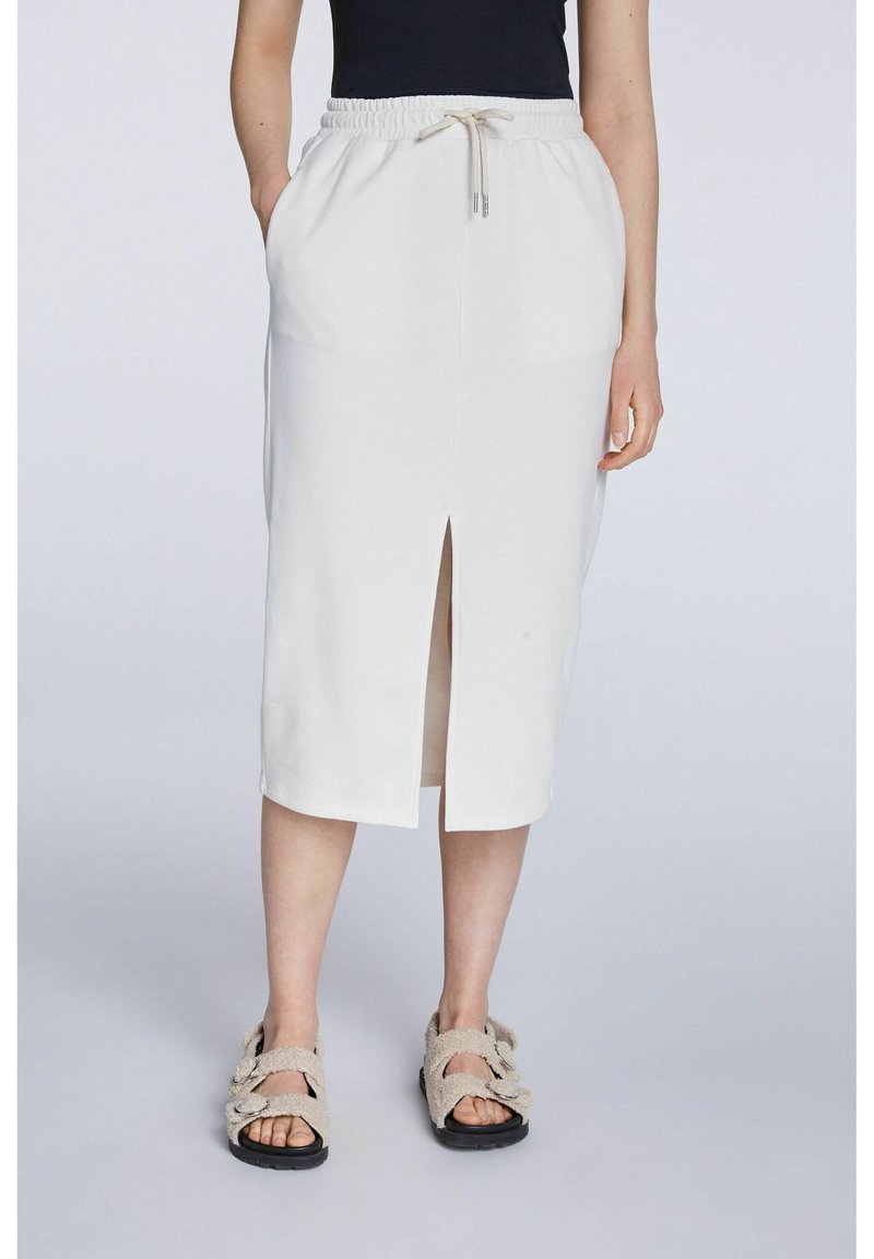 Jupe midi blanche en tissu doux et extensible, avec une taille à cordon de serrage et une fente devant. Associée à des sandales beiges texturées.