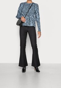 Maglietta a maniche lunghe con motivo astratto blu e nero, abbinata a pantaloni neri a zampa e stivaletti alla caviglia, con una borsa a tracolla.