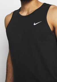 Mies, joka pitää yllä mustaa hihattomaa Nike-paitaa, jossa on valkoinen Nike-logo rinnassa. Paita on leikattu kaulan ja hartioiden kohdalta.