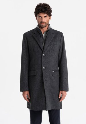 Gray, wool-blend overcoat with a textured pattern, notch lapels, two front pockets, and three buttons. Worn over a gray zip-up jacket.