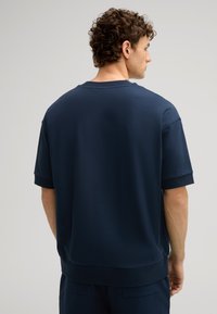 Marineblauwe sweatshirt met korte mouwen, voorzien van een ronde halslijn, ribbelmanchetten en een gladde textuur, weergegeven vanuit de achterkant.