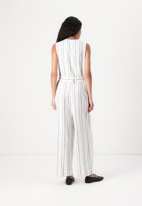 Lett, stripete jumpsuit i hvitt, med blå vertikale linjer. Har en tettsittende midje, vide ben og belte på ryggen. Svarte flate sko.