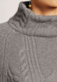 Grauer gestrickter Rollkragenpullover mit geripptem Muster und Zopfmuster an den Schultern. Aus einem weichen, gemütlichen Stoff gefertigt.