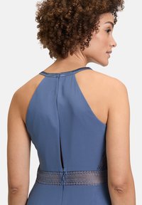 Niebieska sukienka bez rękawów z wysokim dekoltem, satynowym wykończeniem szyi i koronkowymi detalami w talii. Gładki materiał o subtelnej satynie.