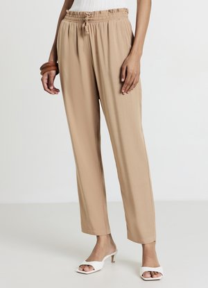 Pantalon beige léger avec taille élastique et cordon de serrage. Coupe droite, texture lisse, assorti à des mules blanches à talons.