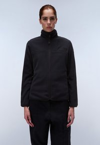 Giacca in pile nera con colletto alto, zip frontale, tasche laterali e rifiniture a contrasto. Include una patch con il logo sul petto.